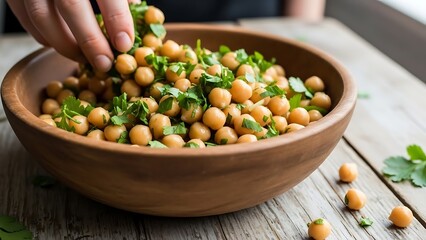A hand scooping chickpeas from a wooden bowl on a table