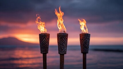 Burning tiki torches illuminate a tranquil beach scene at sunset