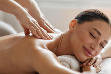 Satisfied lady enjoying back and shoulder massage, spa therapist doing general body massage to young woman, closeup