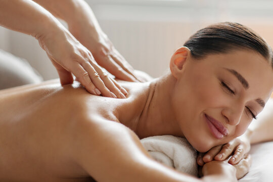 Satisfied lady enjoying back and shoulder massage, spa therapist doing general body massage to young woman, closeup