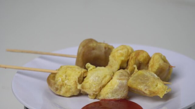 Indonesian street food "Cilor" with egg on skewers served with chili sauce. Authentic traditional snack on a rotating white plate. Popular Asian culinary culture and tasty snack photography. High qual