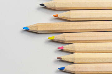 A high-angle, close-up shot of a group of natural wood colored pencils with various colored tips, arranged in a row on a white textured paper background