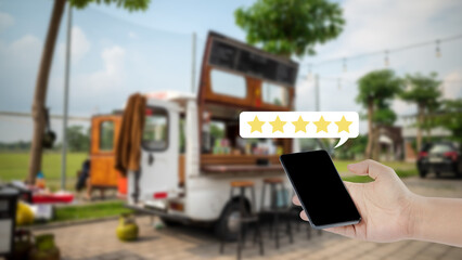 Close-up of a hand holding a smartphone with a five-star rating overlay against a blurred food truck background, representing customer feedback and excellent service reviews