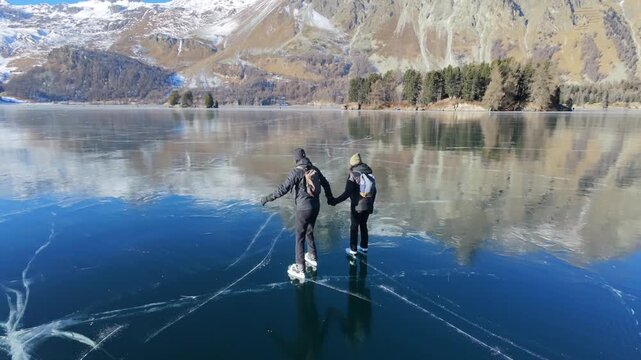 A couple iceskating on a Black Ice Magic Lake, Switzerland, Cinematic Drone 4K