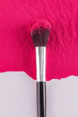 Close-up of cosmetic makeup brush lying on a bright spot of loose pink blush. vertical top view. The concept of beauty and decorative cosmetics