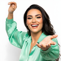 Joyful young brunette woman smiling with left arm raised high and hand open, dressed in a silky light green blouse, against a white background, evoking excitement, celebration, or success vibes.