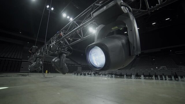 Brightly glowing spotlight hangs on frame over empty stage closeup. Powerful lighting equipment for musical band performance in concert hall