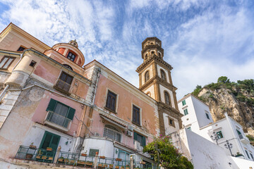 Fototapeta premium Amalfi Coast, Italy, Atrani. Historic building with a tall bell tower of Church of Santa Maria Maddalena and colorful facades under a blue sky, showcasing architectural details and hillside backdrop