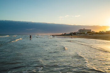 A beach scene with people swimming in the ocean and a cloudy sky