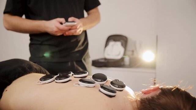 Person lying on stomach receiving electric muscle stimulation for pain relief and recovery. Professional doctor operating modern health tech