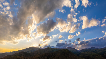 Majestic mountains rise under dramatic clouds during late afternoon. Serene landscape captures nature's beauty and tranquility in golden light.
