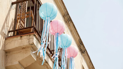Colorful paper lanterns with flowing ribbons hang from a balcony as festive party decorations glowing in daylight