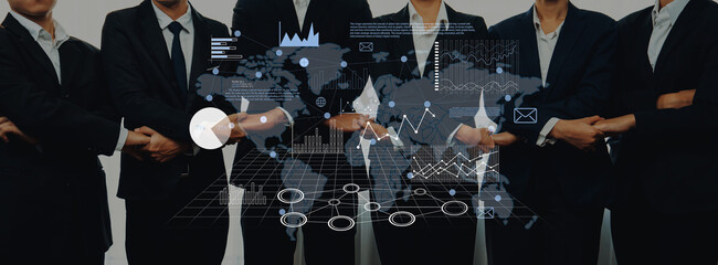 A group of business professionals in suits standing confidently, with an overlay of digital graphics representing a world map and financial statistics. Trope