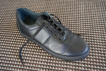 one black leather sneaker, Black leather shoes standing on a textured surface