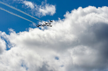 Formation of nine fighter jets flying into clouds in a blue sky