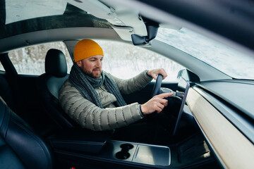 Man driving electric car in winter adjusting screen