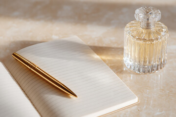 elegant desk arrangement, elegant still life with an open linen notebook, gold fountain pen, and crystal decanter on a light beige marble surface, softly illuminated plenty of negative space