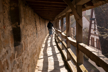 Historic covered walkway along stone wall with wooden railing
