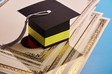 stack of blank certificate and  mortarboard on blue background.