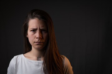Naklejka premium Confused and angry young caucasian woman in dramatic dual-lit studio portrait