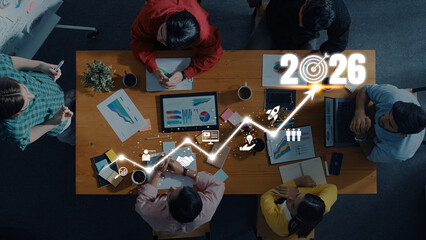 A diverse team collaborates in a modern workspace, analyzing data charts and exploring growth projections for 2026. The setting highlights teamwork and innovation. Trope