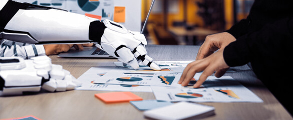 A robotic arm collaborates with a human in analyzing business reports and data visualizations in a modern office setting, enhancing productivity and innovation.Noogenesis