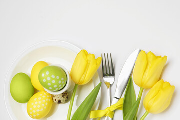Easter celebration. Festive table setting with tulip flowers, painted and quail eggs on white...