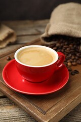 Obraz premium Cup with aromatic coffee and beans on wooden table against black background, closeup