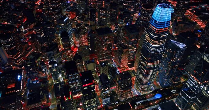 Flying above the blue neon top of Salesforce Tower in the downtown San Francisco. View of the vibrant lively city from drone at night.