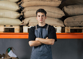 Confident male worker with arms crossed against shelves. Young warehouse worker looking at camera.