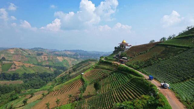 Aerial drone footage of a beautiful agricultural valley with colorful hills, a gold roof mosque, a blue trike moving ,in the touristic spot of Panyaweuyan, Majalengka regency, Java island, Indonesia