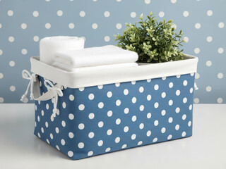 Blue polka dot storage basket with white towels and green plant