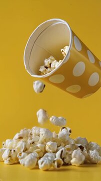 Slow-motion vertical video of classic popcorn falling against a bright yellow background. Perfect for cinema-themed stories, food advertisements, or snack-related design templates.