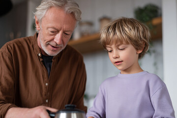 Elderly man and young boy are preparing food together in home kitchen. Grandfather and grandson share a moment of learning and connection