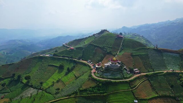 Aerial drone footage of an agricultural valley with green hills, a gold roof mosque, a countryside road, food stalls, in the touristic spot of Panyaweuyan, Majalengka regency, Java island, Indonesia