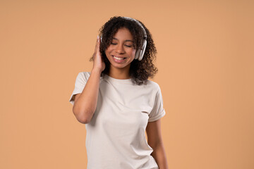 African Teen Girl Listening Music, Enjoying Songs, Headphones On Beige Backdrop