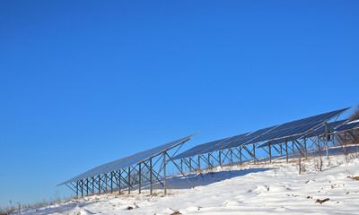 Photovoltaic batteries covered with snow against a background of a saturated sky. Solar panels in the countryside. Alternative energy concept. Energy crisis.