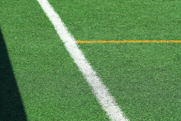 Green synthetic grass, artificial turf sports field with yellow and white lines. Sport stadium in sunny day