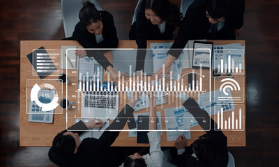 A diverse team of professionals collaborates over reports and charts in a modern office, enhanced by a digital overlay showcasing analytics and data visualization. Trope