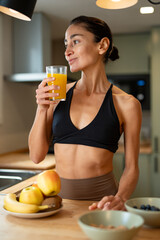 Athletic woman drinking fresh orange juice in modern kitchen, healthy breakfast with fruit and...