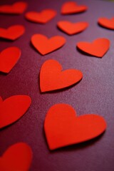 Scattered bright red heart shapes resting upon a deep burgundy surface