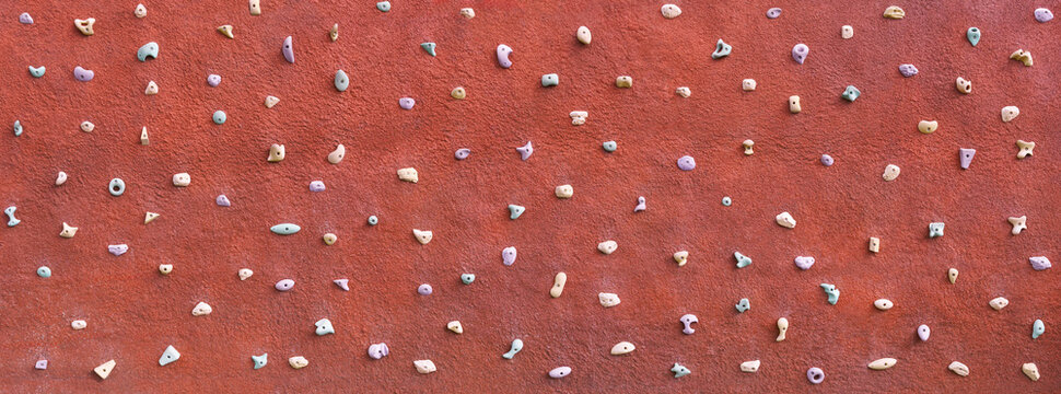 Kletterwand Panorama Hintergrund - viele kleine Griffe f&uuml;r Kinder an einer roten Wand mit grobem Verputz im Freien, Teil eines Spielplatzes