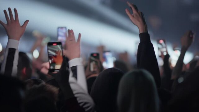 Crowd of fans films live music performance on smartphones in dark concert hall with stage lights