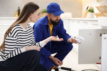 Fototapeta premium Young woman talking with plumber in kitchen