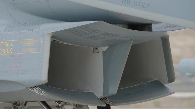 Close-up of military jet underfuselage air intake showing variable cowl emergency entrance markings and caution instructions