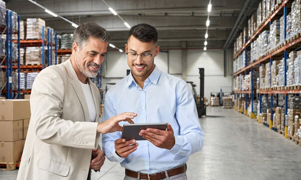 Warehousing and Distribution. Team of two happy professional warehouse managers working with system management standing in storage using digital tablet. Logistics, shipping, and retail distribution. - Powered by Adobe