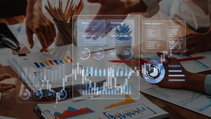 A business team collaborates in an office setting, analyzing financial data and charts displayed on digital devices, emphasizing teamwork and strategic insights. Raster