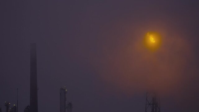 Industrial smokestack flaring off excess gas in fog.