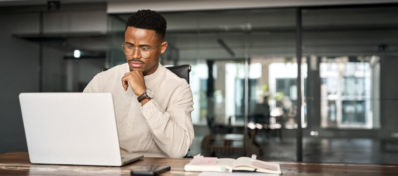Busy professional African business man company employee, young male businessman looking at computer thinking on online investment or software technology using laptop working at office. Copy space.