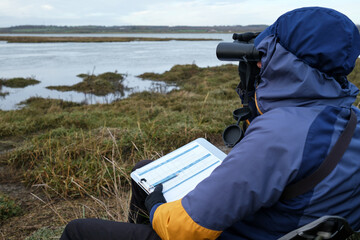 Field Scientist Using Binoculars for Wildlife Observation and Ecological Restoration Project Monitoring